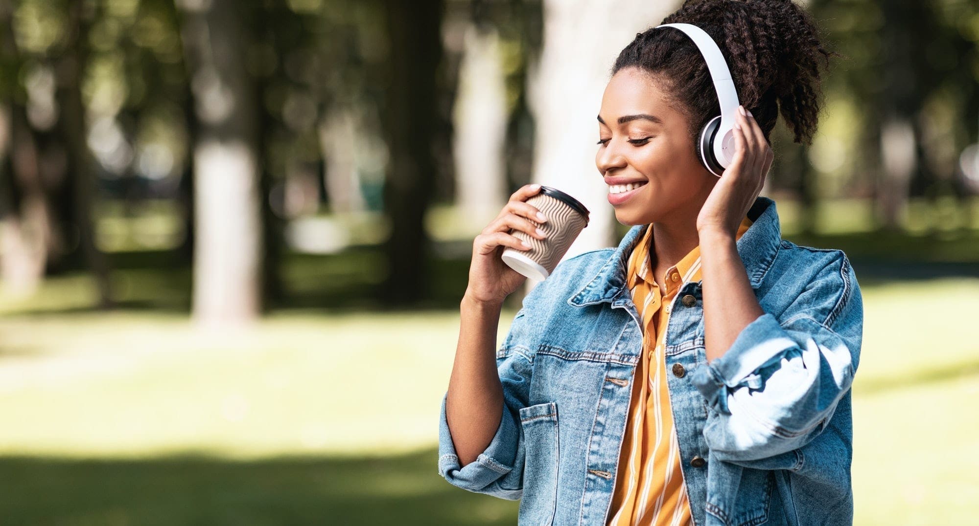 African Millennial Girl With Headphones Having Coffee Walking Outside, Panorama