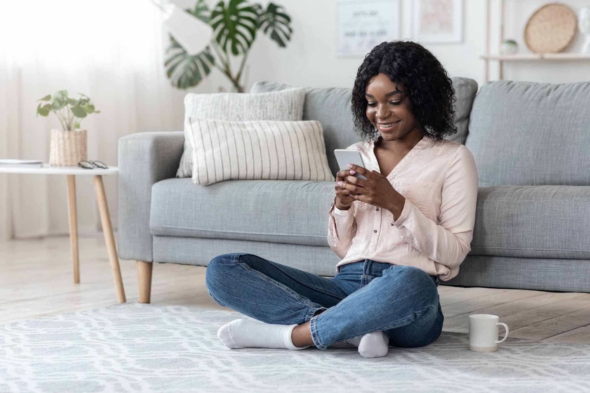 African Woman Browsing Social Media On Smartphone And Drinking Coffee At Home