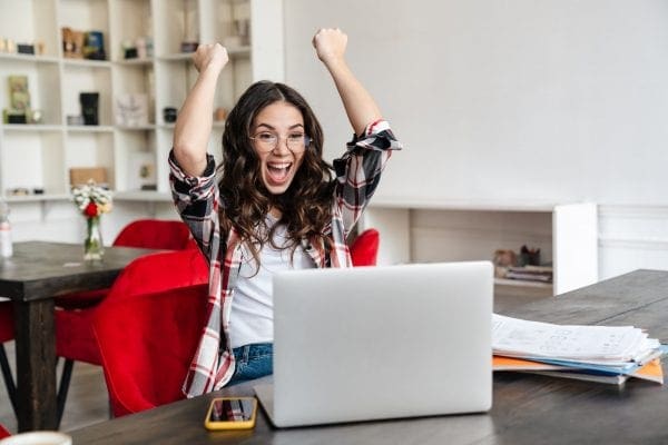 Excited nice woman making winner gesture while working with laptop