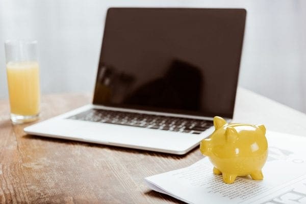 yellow piggy bank and laptop with blank screen at table