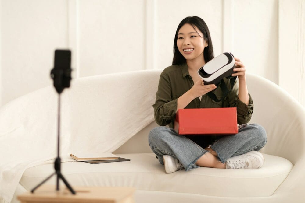 Asian woman influencer opening parcel and streaming, showing VR headset