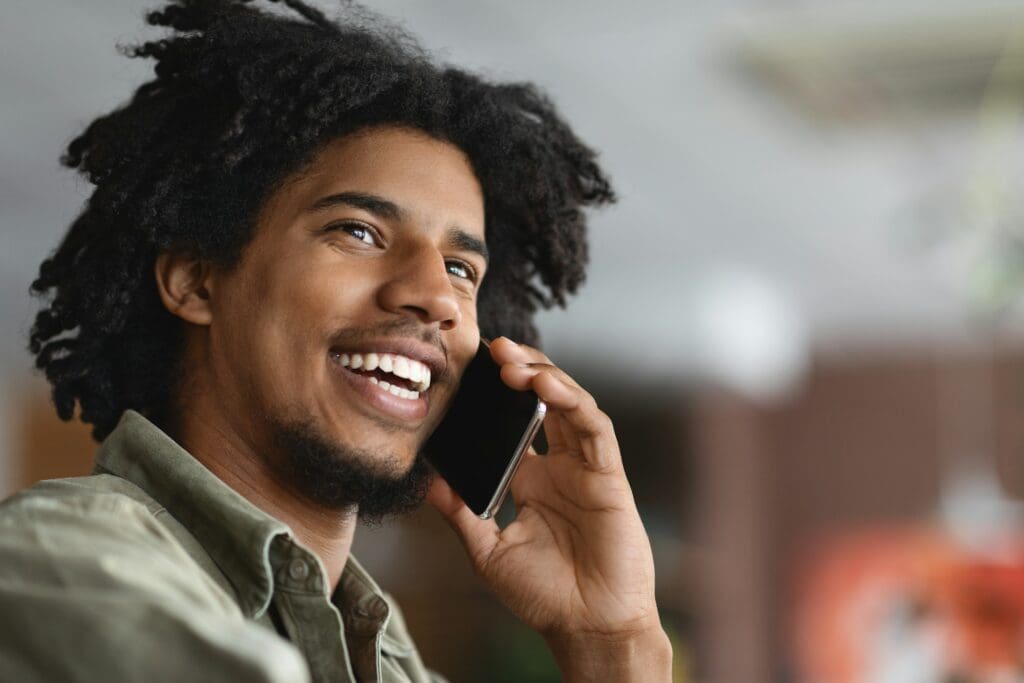 Mobile Call. Closeup Shot Of Smiling Black Guy Talking On Cellphone Indoors