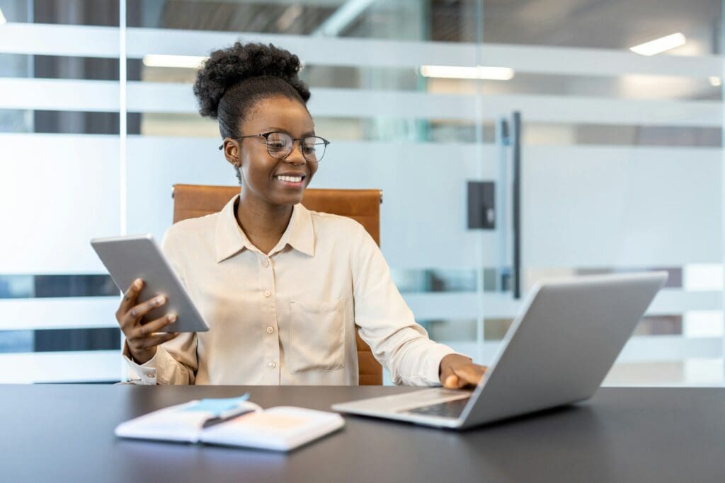 Smiling businesswoman using digital tablet and laptop in modern office