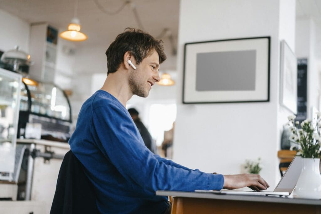 Smiling man in a cafe with earphone using laptop