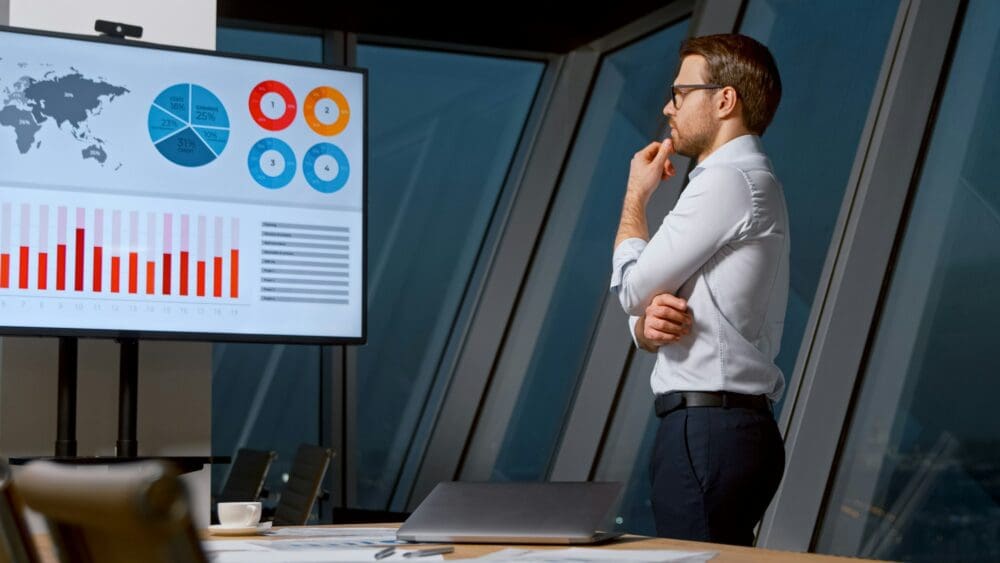 Thinking young man looking at screen with analytics in meeting room