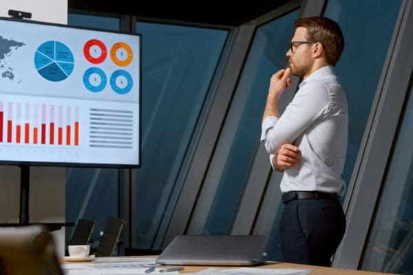 Thinking young man looking at screen with analytics in meeting room